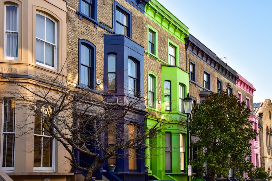 A row of multi-storey Victorian houses in Notting Hill painted in various pastel shades, including blue, teal, white, and pink, with bay windows and small front gardens separated by wrought iron fence