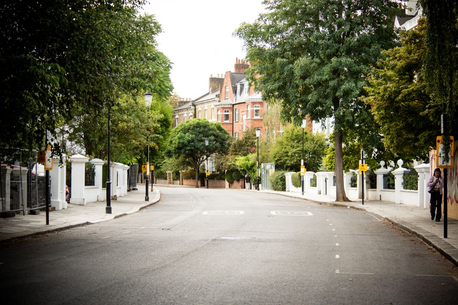 Photograph of a row of colorful terraced houses on a residential street during daytime, featuring pastel facades in shades of blue, yellow, and lavender. Each property has black wrought iron railings,